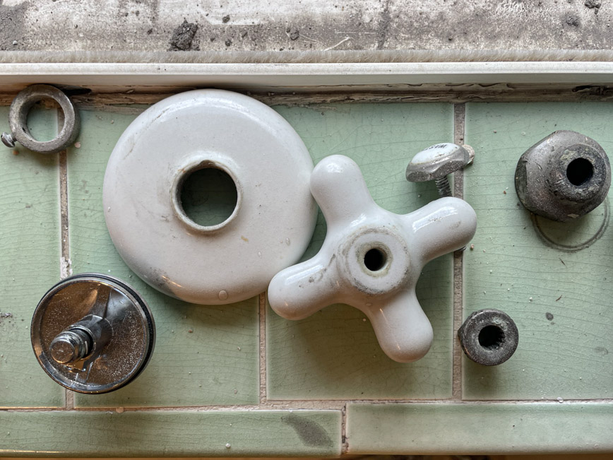 Bath faucet parts spread apart on a dark surface, photographed in low industrial light.